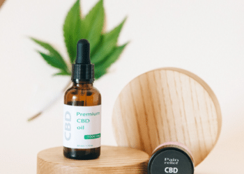 Hemp-derived CBD oil and topical product containers displayed with hemp leaves on a wooden platform