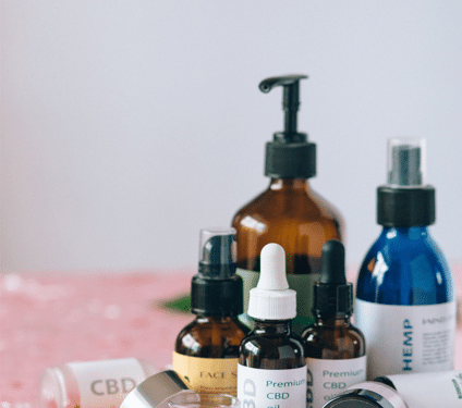 Hemp-derived CBD oils, topical creams, capsules, and other cannabinoid wellness products arranged on a pink surface.