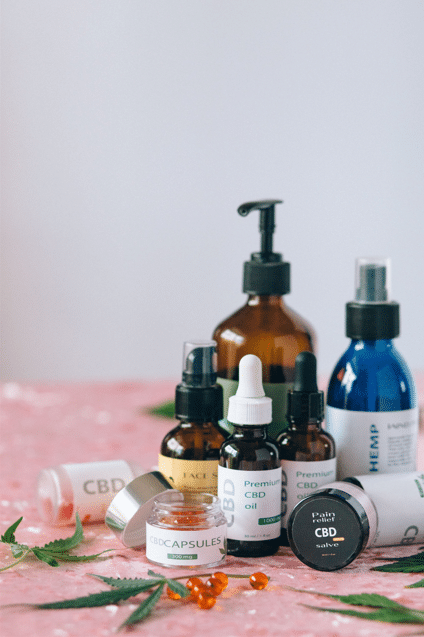 Hemp-derived CBD oils, topical creams, capsules, and other cannabinoid wellness products arranged on a pink surface.
