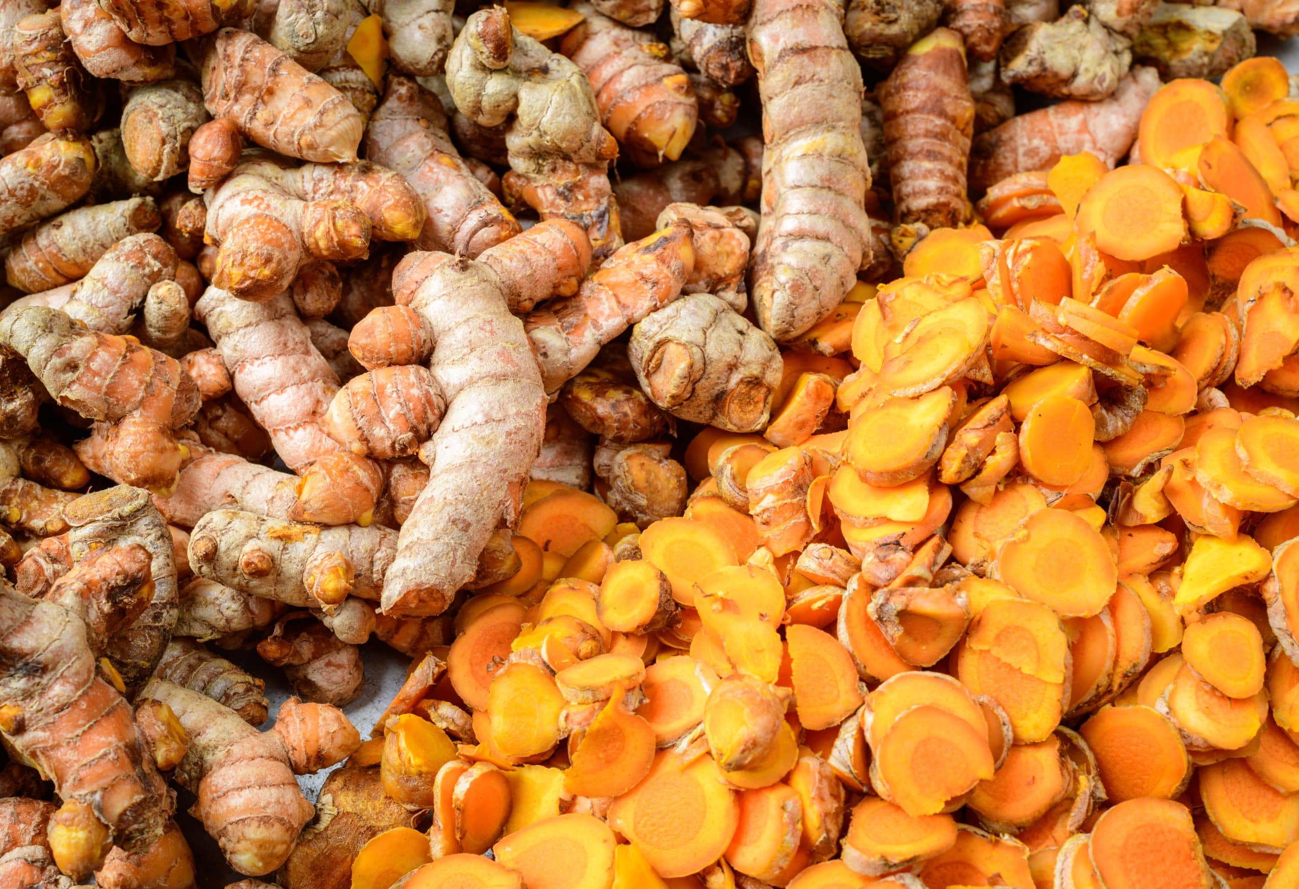 Fresh Turmeric roots and turmeric slices (Curcuma longa) close up, cut into little slices for drying up in the sun, the process for making turmeric powder spice,