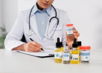 partial view of african american doctor with stethoscope holding bottle with medical cannabis