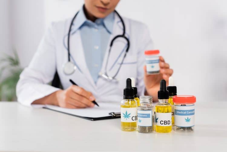 partial view of african american doctor with stethoscope holding bottle with medical cannabis
