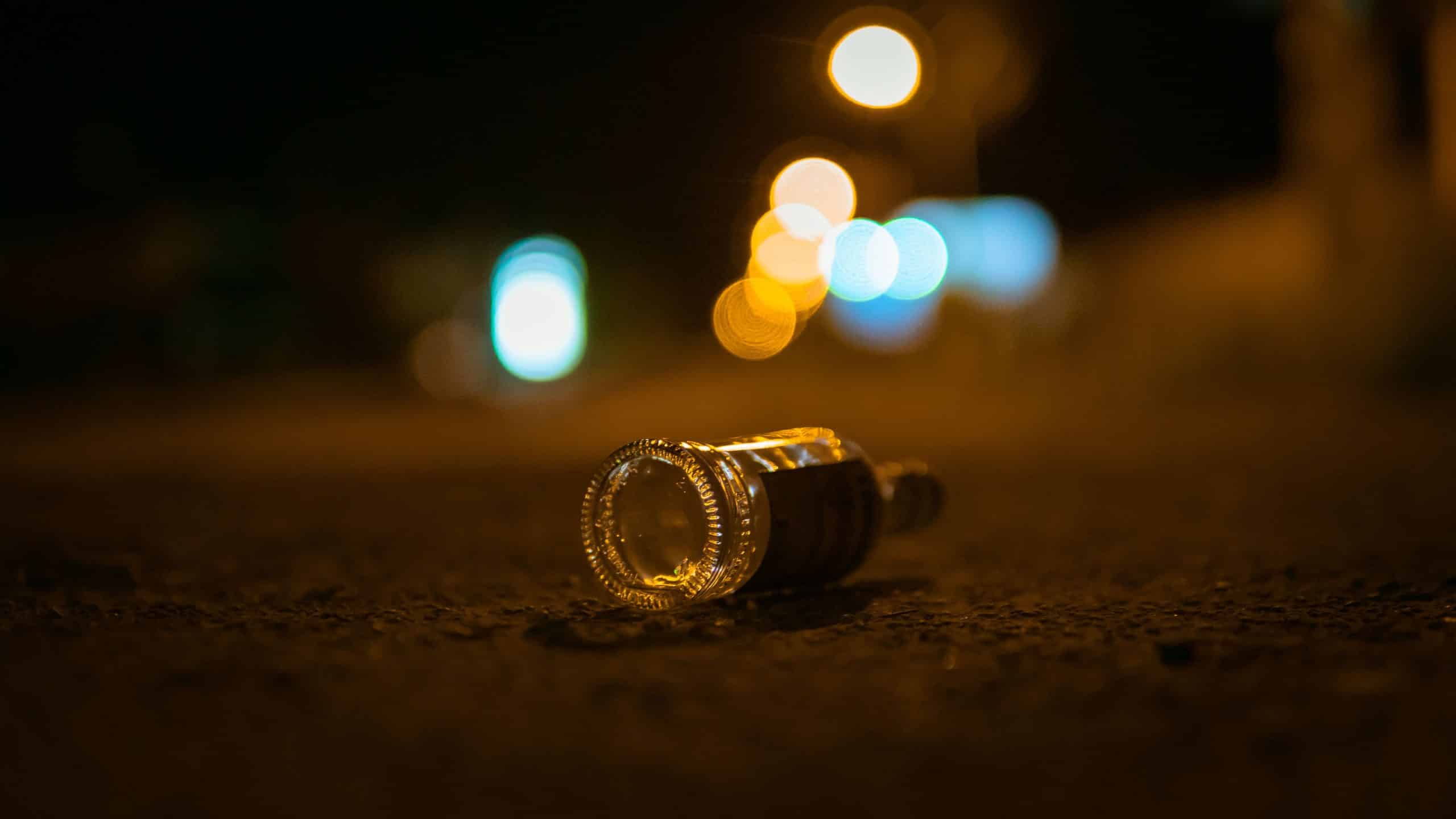A selective focus shot of empty bottle of alcohol thrown in the middle of street on bokeh background